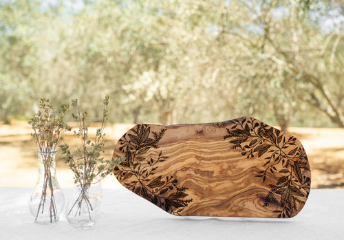Rustic olive wood serving board with botanical design on a table outdoors