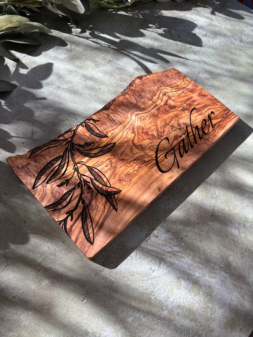 Rustic live-edge olive wood serving board engraved with an olive leaves design