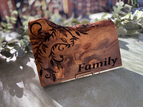 Angled close-up of the Family lettering and botanical engraving on an olive wood board