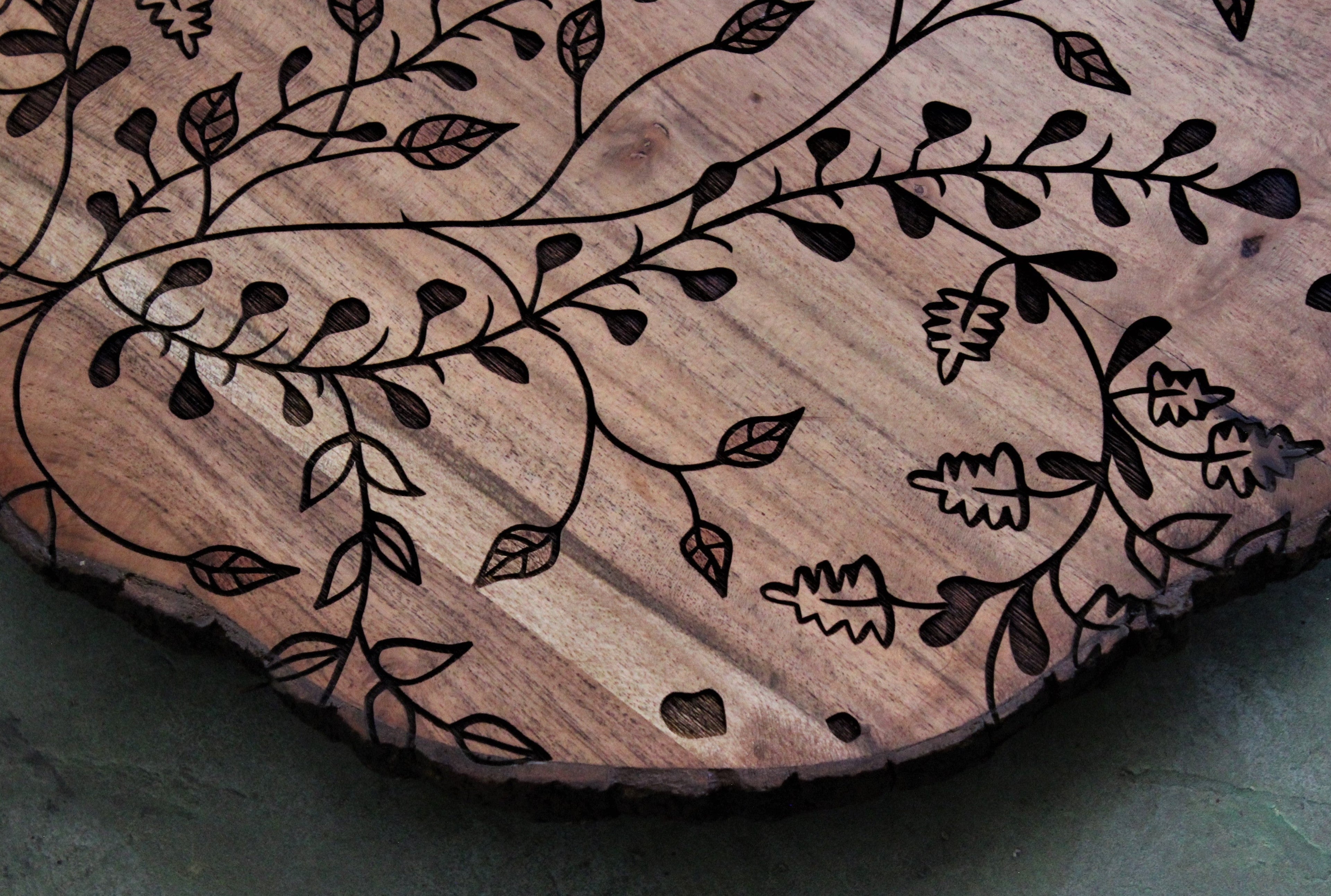 Wooden cutting board with engraved floral patterns on a gray surface